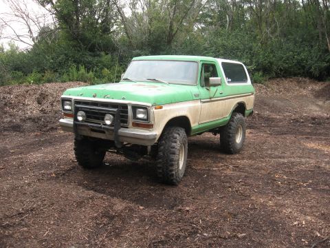 1979 Ford Bronco - This lifted 1979 Ford Bronco is shown in a three-quarter front view, parked on a dirt lot with trees in the background.