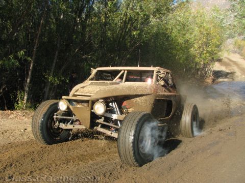 1990 Ford Bronco - mud-coated off-road buggy with round front lights accelerates along a dirt trail, raising tire smoke.