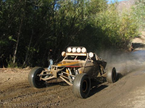 1990 Ford Bronco - tube-frame off-road race buggy with a four-light roof bar speeds down a dirt road while a bystander watches from the brush.
