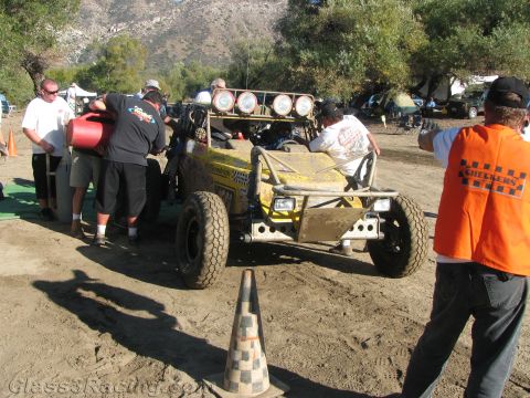 1990 Ford Bronco - Crew members service a yellow tube-frame off-road buggy in a dirt pit while an official in an orange Checkers vest stands nearby.