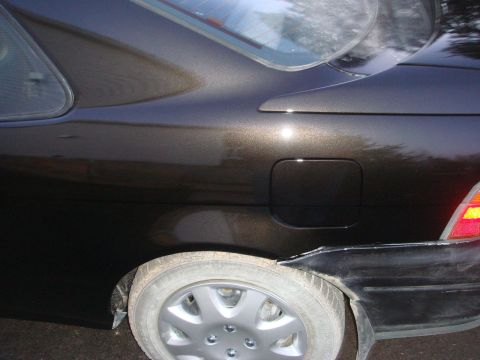 1996 Ford Bronco - Rear view of a dark metallic car showing the quarter panel, fuel door, and a damaged bumper.