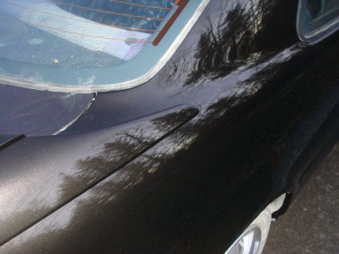 1996 Ford Bronco - The rear quarter panel of a black vehicle shows reflections of trees in its glossy paint.