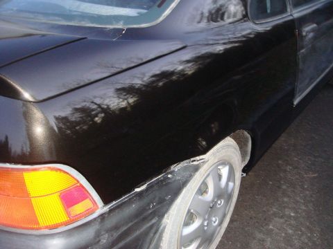 1996 Ford Bronco - The rear of a black car shows damage to the bumper and a partially visible taillight.