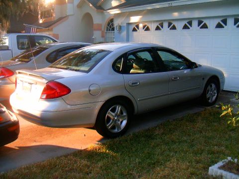 2002 Ford Taurus - A silver sedan is parked in a driveway next to a garage and another vehicle.