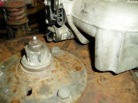 2000 Ford E350 - A detailed view of an engine component, likely a sensor, adjacent to a heavily rusted hub assembly.