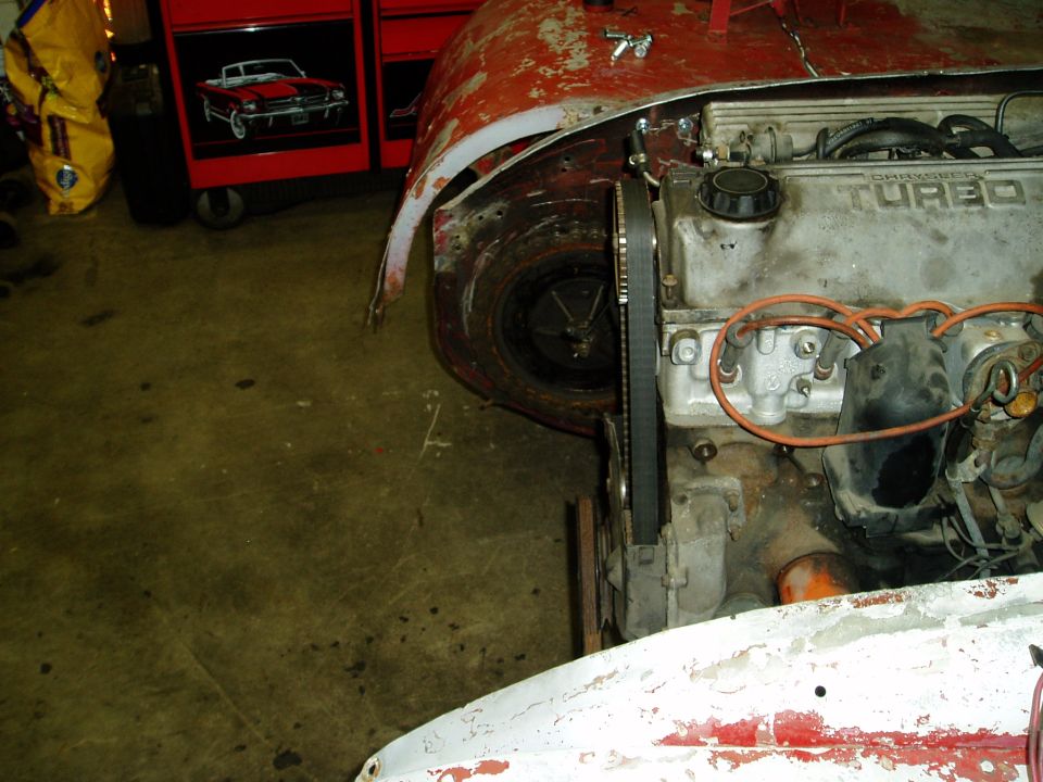 Engine and wheel well of a red vehicle under repair, with a "SUPERMOTORS" watermark