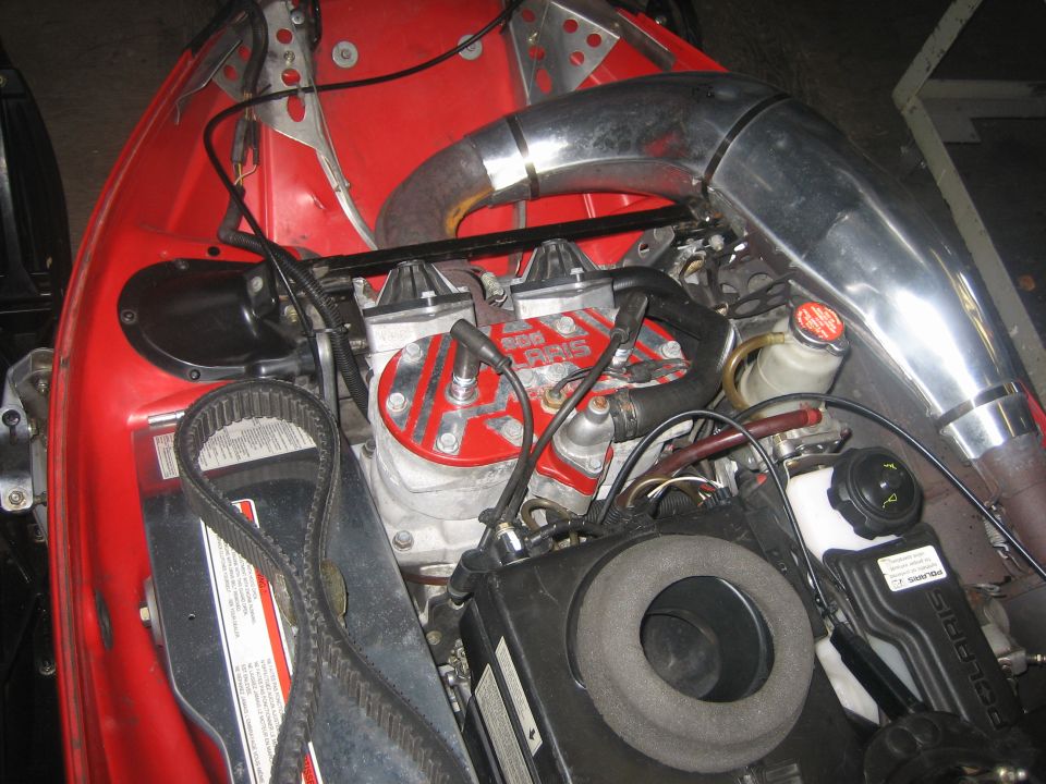 Red snowmobile engine with chrome exhaust pipe and visible belt