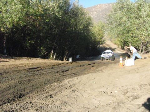 1990 Ford Bronco - white off-road truck sits on a rutted dirt trail in the distance with an orange cone and a person marking the foreground.