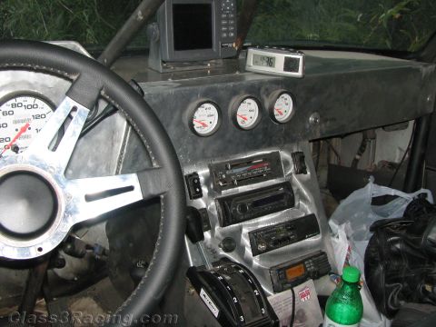 1990 Ford Bronco - metal dashboard of an off-road race vehicle holds a speedometer, three auxiliary gauges, stacked radios, a nav unit and a shifter.