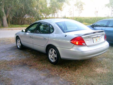 2002 Ford Taurus - This silver 2002 Ford Taurus sedan is shown from the rear 3/4 angle, with another vehicle partially visible in the background.