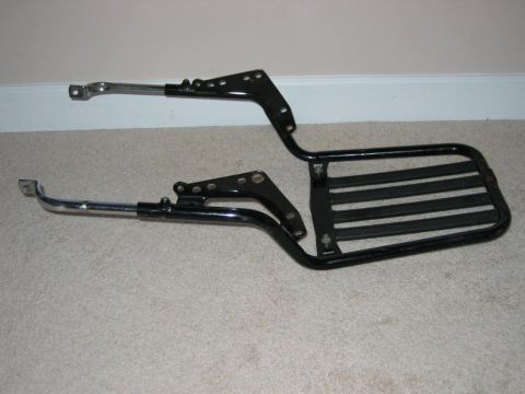 1985 Ford LTD Crown Victoria - A black metal luggage rack with chrome mounting arms and rubber slats is shown against a carpeted floor and white baseboard.