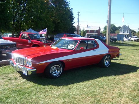 1975 Ford Torino - Red and white 1975 Ford Torino coupe parked on grass with other vehicles in the background.