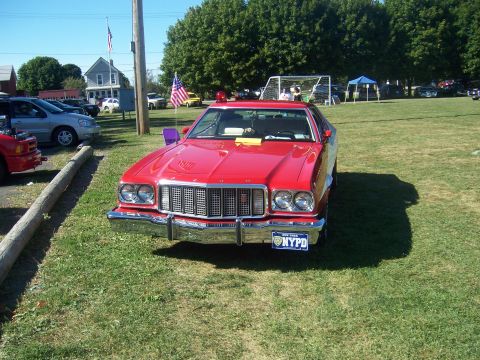 1975 Ford Torino - This red vehicle, marked as NYPD, is parked on a grassy field under a clear sky.