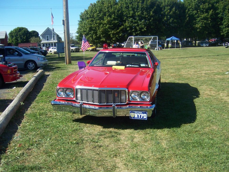 Red NYPD police car parked on grass, front view. Has a light bar on top