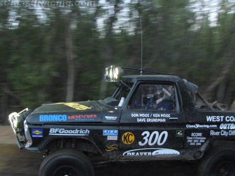 1990 Ford Bronco - black number 300 Ford off-road race truck speeds along a dirt trail, its side covered in BFGoodrich, KC and Bronco Driver decals.