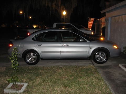 2002 Ford Taurus - A silver sedan is parked in a driveway at night, with a white truck behind it.