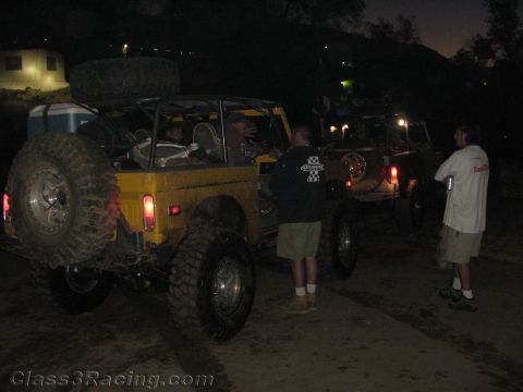1990 Ford Bronco - yellow open-top off-road vehicle with a spare tire is staged at night while several people stand around it.