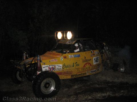 1990 Ford Bronco - heavily decaled yellow off-road race buggy numbered 1405 races through a dark course with twin roof lights at night.