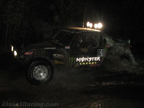 1990 Ford Bronco - dark off-road race buggy lettered BC-16 with Monster Energy and KMC graphics climbs a rough dirt course at night.