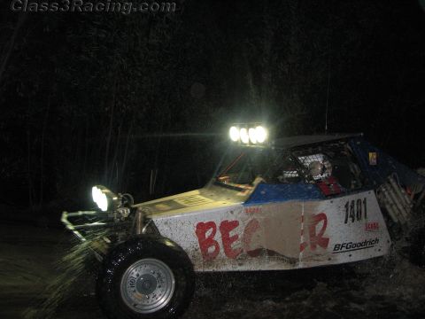 1990 Ford Bronco - white-and-red off-road race buggy numbered 1401 and lettered 'Becker' sprays water under its roof light bar at night.