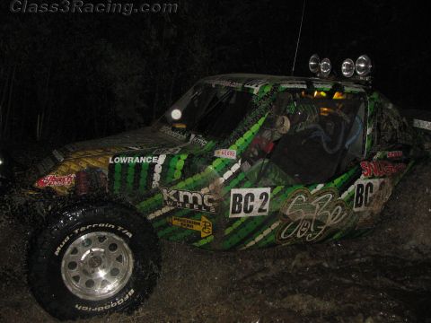 1990 Ford Bronco - green-camo off-road race buggy lettered BC2 with twin roof lights and KMC graphics sits on a dark course at night.
