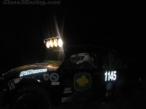 1990 Ford Bronco - dark off-road race buggy numbered 1145 with 'Williams' lettering and a roof light bar sits on a course at night.