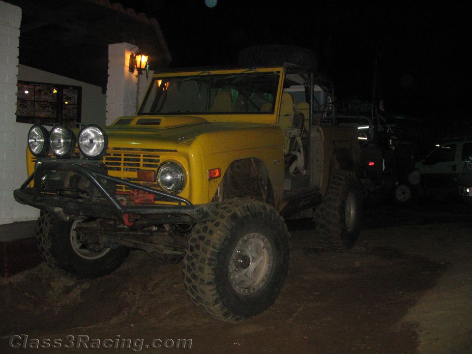 Yellow vintage early Ford Bronco off-road truck parked at night by a building