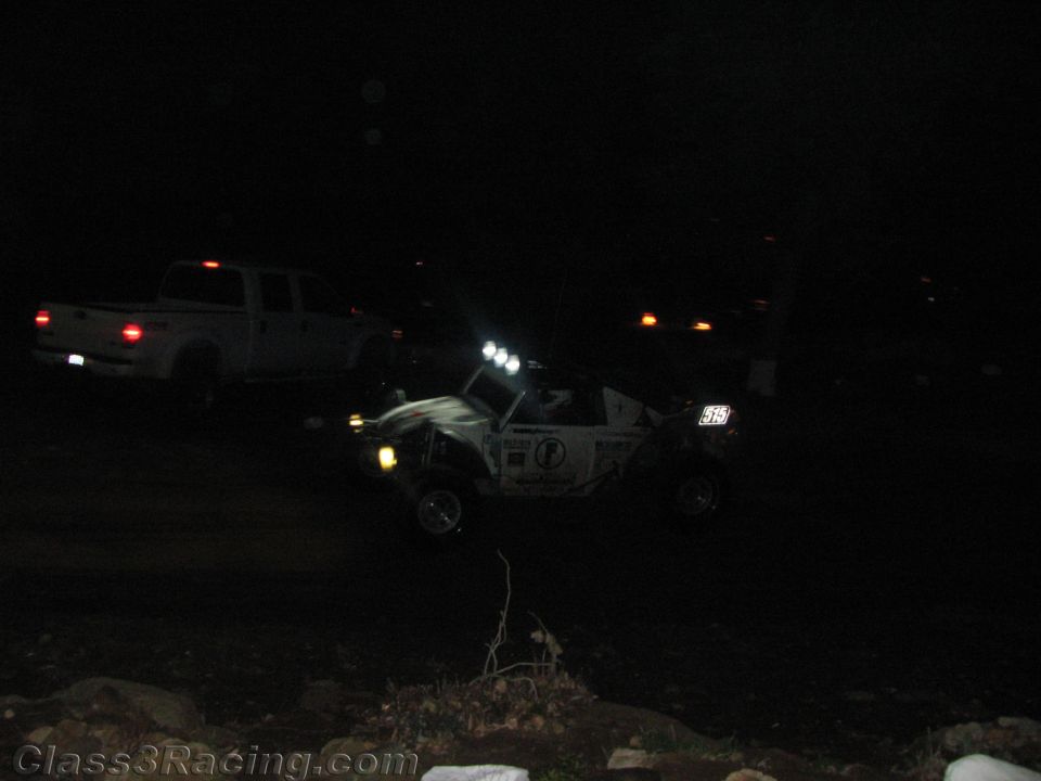 Dimly lit off-road racer with roof lights beside a white pickup at night