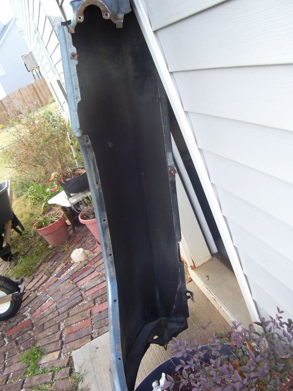 Car fender leaning against a house exterior. Some plants and brickwork are visible in the background