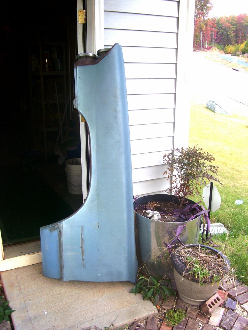 Light blue automotive front fender panel leaning against house siding outdoors
