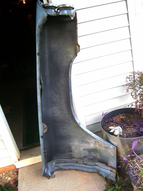 1965 Pontiac Bonneville - A detached car fender is shown leaning against a house, with a potted plant nearby.