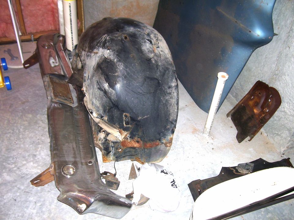 Stripped rusty inner fender and cut body panels stored against a basement wall