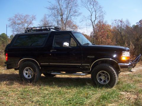 1996 Ford Bronco - Side view of a black 1996 Ford Bronco parked outdoors with trees in the background.