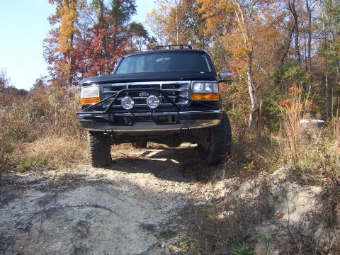1996 Ford Bronco - A black Ford Bronco is parked on a dirt path surrounded by trees with autumn foliage.