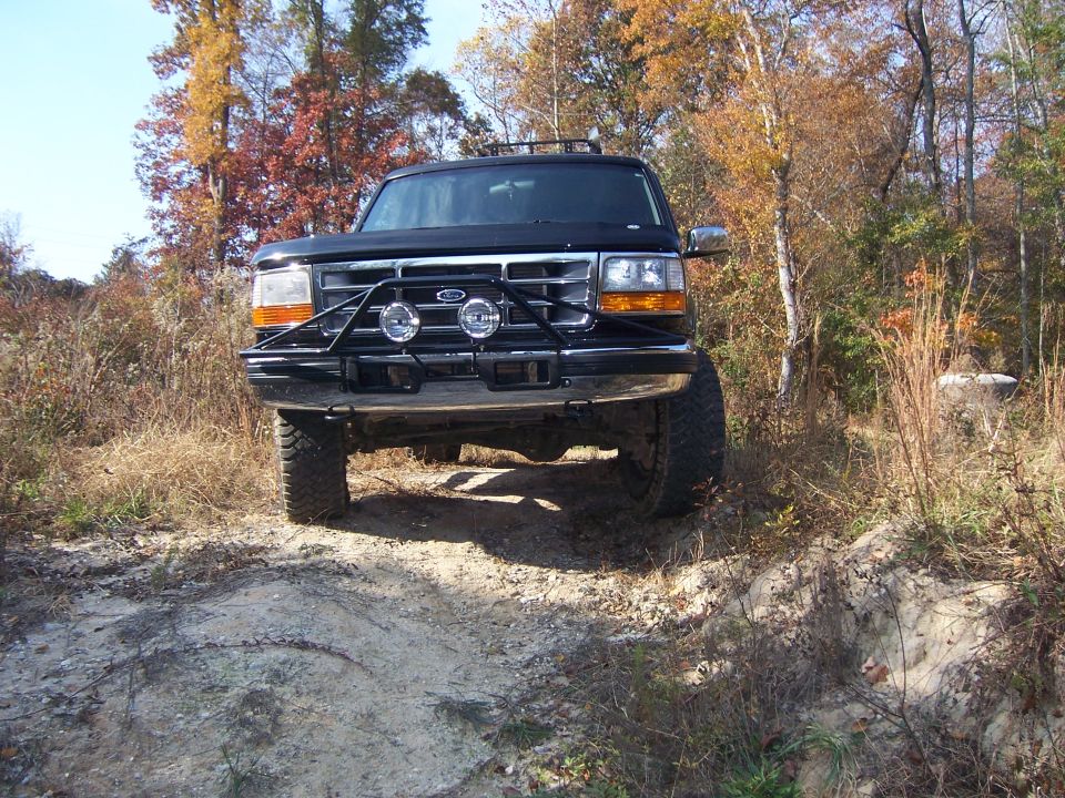 Black Ford Bronco on dirt road, front view. Bull bar with lights attached