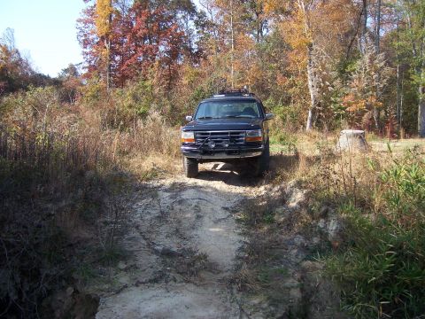 1996 Ford Bronco - Black Ford Bronco navigates a dirt path surrounded by autumn foliage.