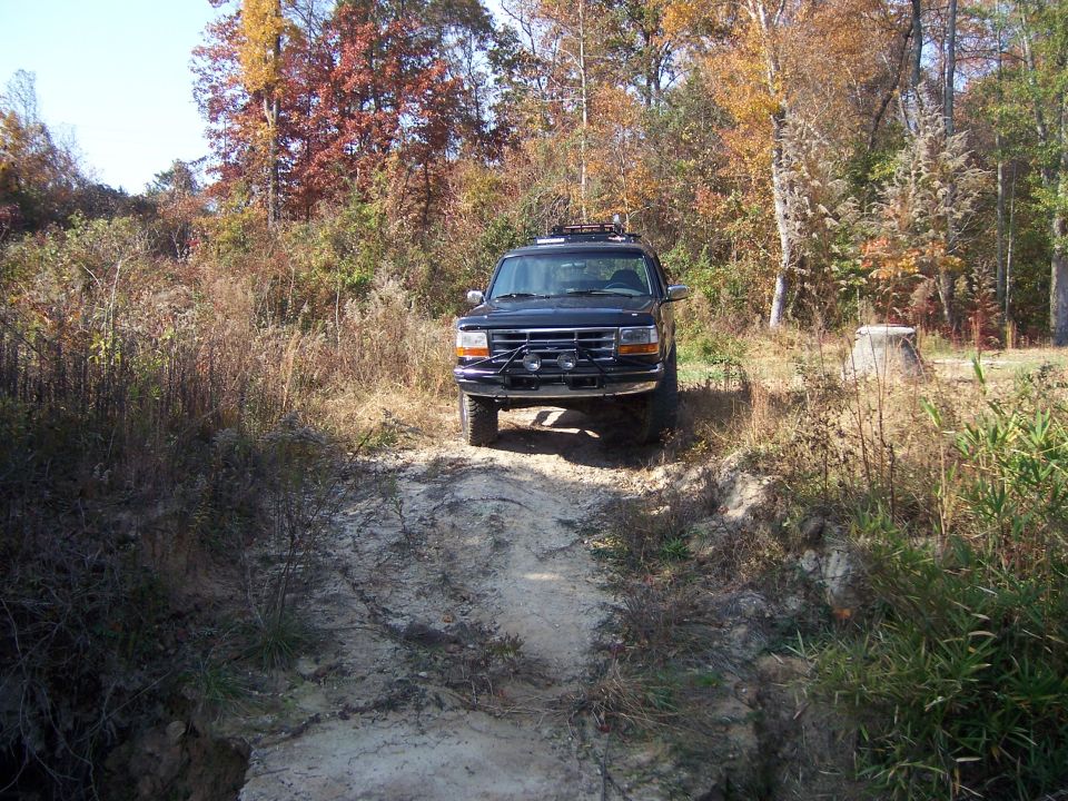 Black Ford Bronco with a brush guard on a dirt path in autumn woods