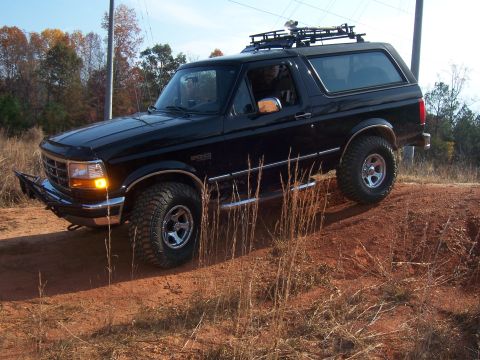 1996 Ford Bronco - Black 1996 Ford Bronco with roof rack is shown off-roading on a dirt hill.
