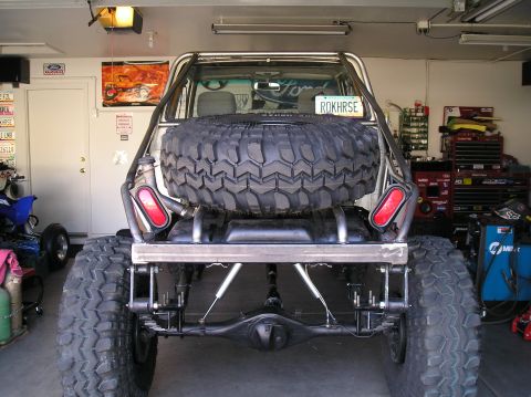 1986 Toyota Hilux - Rear view of a heavily modified truck-based rig with a tube frame/roll cage, spare tire mounted in the rear opening, dual round taillights,…