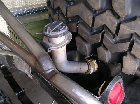 1986 Toyota Hilux - Custom fuel filler neck with a locking-style cap routed through a bare-steel tube frame section, joined to the tank by rubber hose with twi…