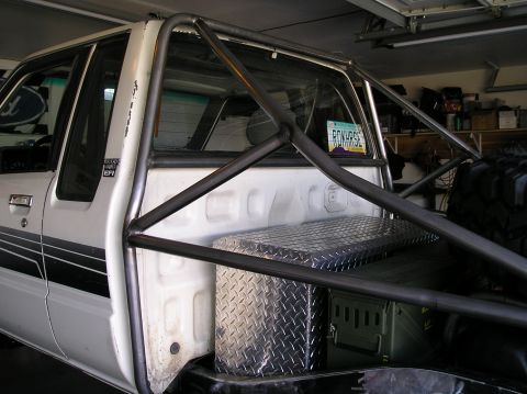 1986 Toyota Hilux - A white pickup truck is shown from the side with a custom roll cage installed in the bed.
