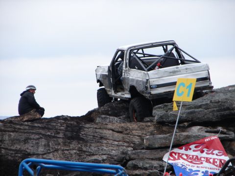 1995 Ford Bronco - A heavily modified SUV navigates a challenging rocky obstacle course, with a spectator observing from the side.
