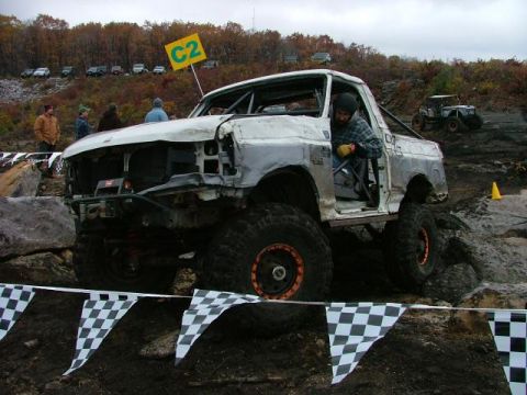 1995 Ford Bronco - This heavily modified truck, likely a 1992 Ford Bronco, is participating in an off-road event with checkered flags and course markers visib…
