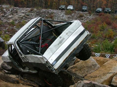 1995 Ford Bronco - A heavily modified Ford Bronco navigates a challenging rock obstacle course with other vehicles in the background.
