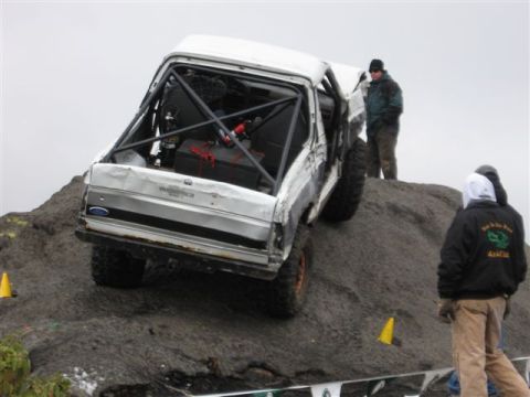1995 Ford Bronco - A heavily modified pickup truck navigates a steep, muddy incline during an off-road event.