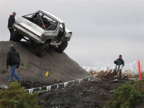 1995 Ford Bronco - An off-road vehicle navigates a steep dirt incline with spectators nearby.