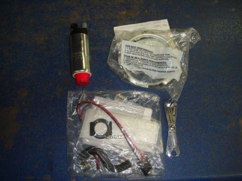 1996 Ford Bronco - A fuel pump replacement kit laid out on a blue surface, including the electric fuel pump with red inlet cap, a bagged strainer/filter with…