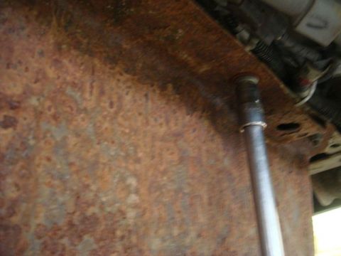 1996 Ford Bronco - Close-up underside view of a heavily rust-covered metal surface, likely a frame or body panel, with a metal rod or shaft passing through a…