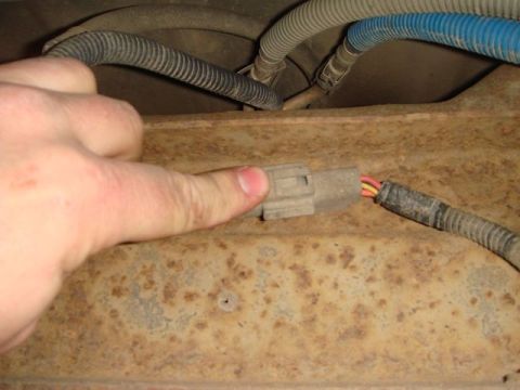1996 Ford Bronco - A hand holds a weathered gray two-pin electrical connector near an unplugged mating harness with yellow and pink/red wires, set against a r…