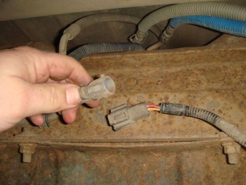 1996 Ford Bronco - A hand holds a two-pin electrical connector near its matching mating plug with red and yellow wires, positioned over a heavily rusted metal…
